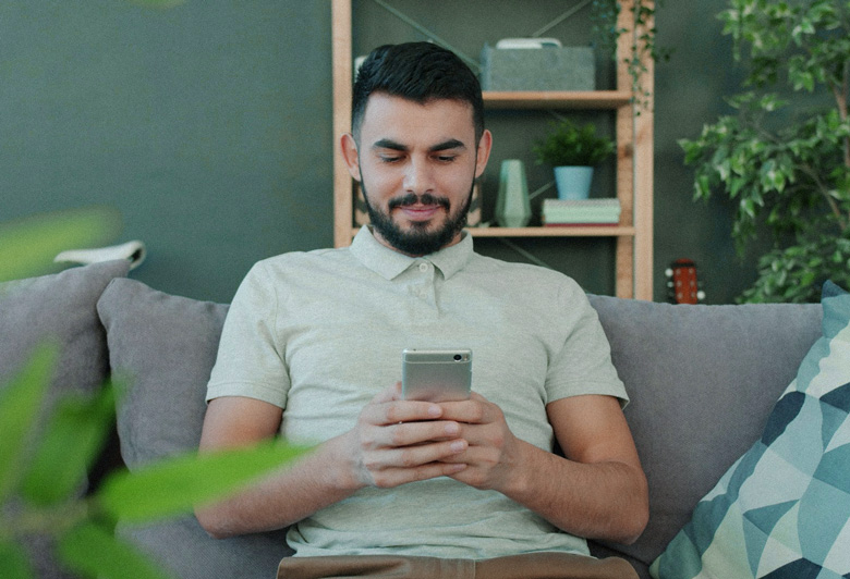 Man smiling while using his smartphone on a grey sofa at home