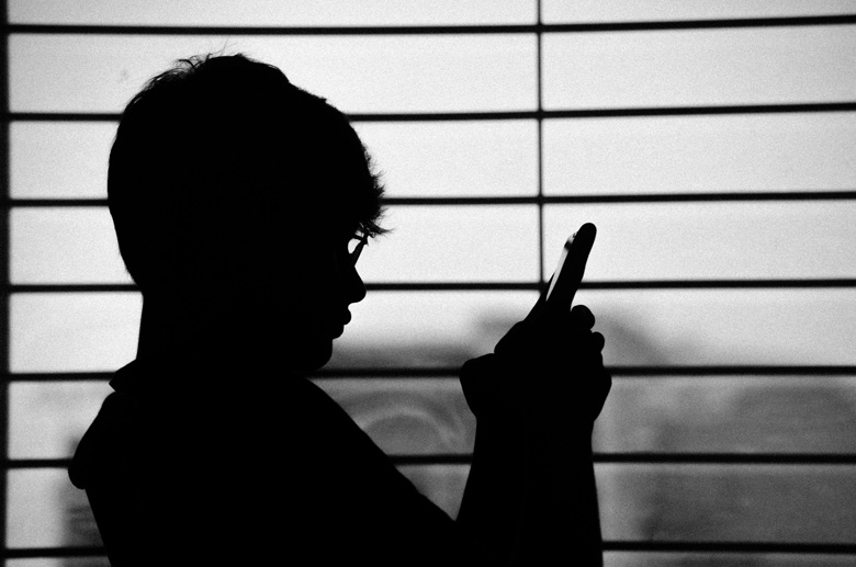 ظل شخص ينظر إلى شاشة الهاتف بجانب ستارة نافذة أفقية